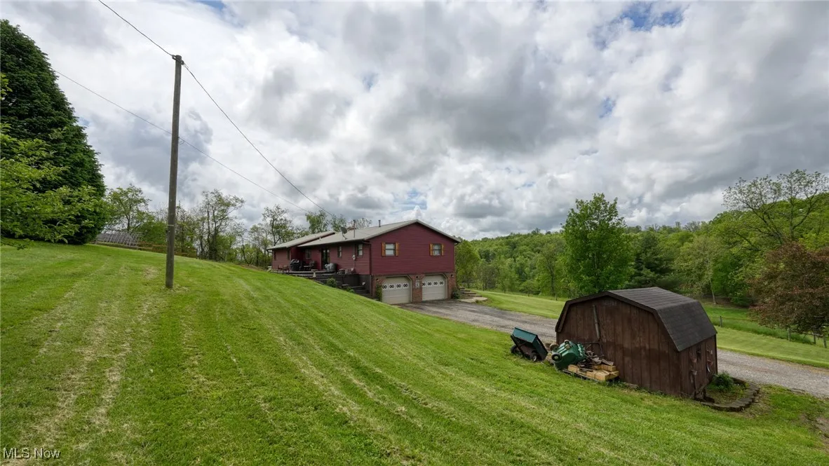 View of green lawn featuring asphalt driveway, a garage, a shed, and an outbuilding