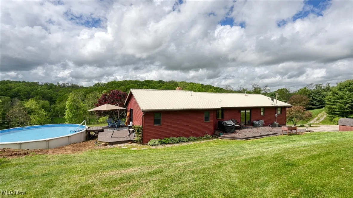 Back of house featuring a deck, an outdoor pool, a lawn, and a chimney