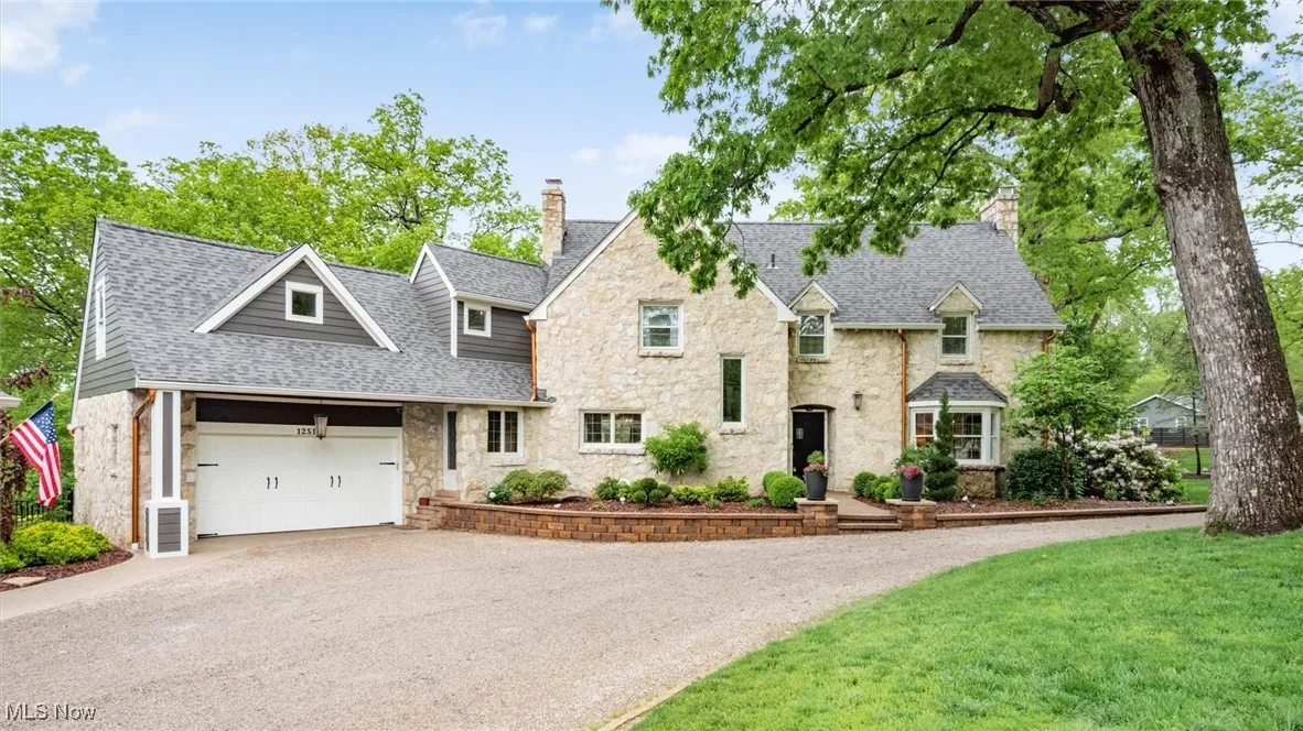 View of front facade with a chimney, stone siding, driveway, a garage, and roof with shingles