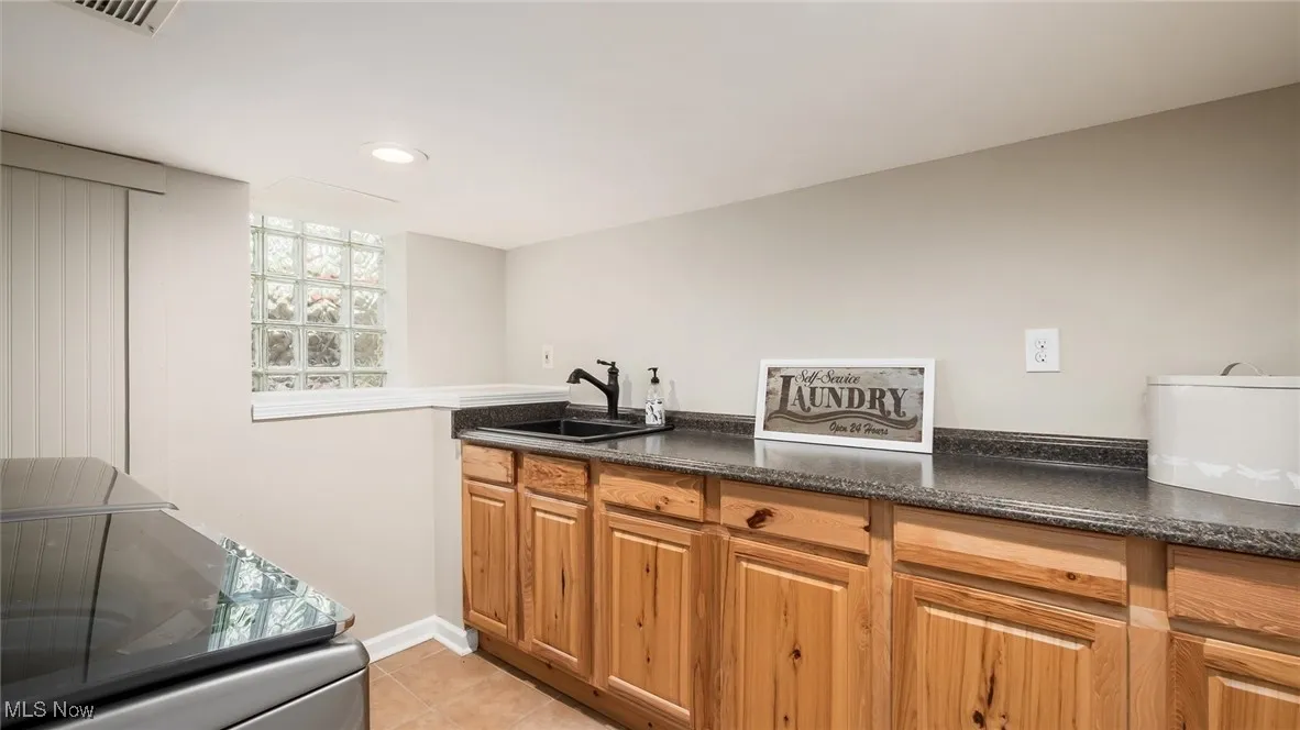 Kitchen with a sink, light tile patterned flooring, brown cabinets, recessed lighting, and baseboards