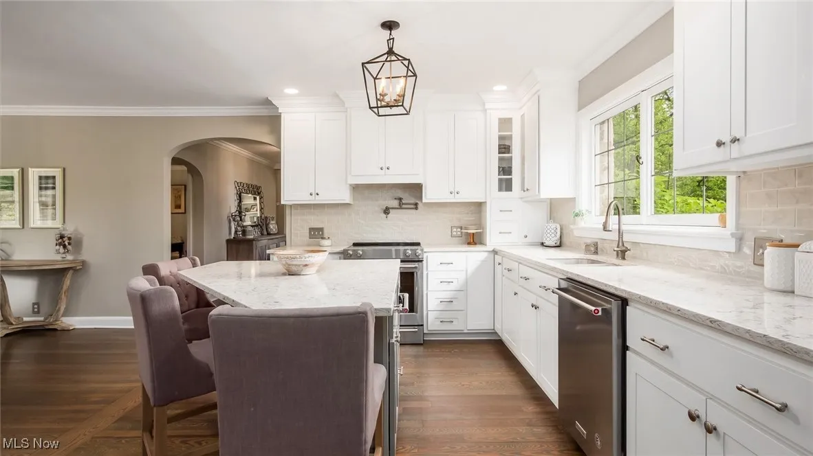 Kitchen featuring stainless steel appliances, a sink, crown molding, arched walkways, and white cabinetry
