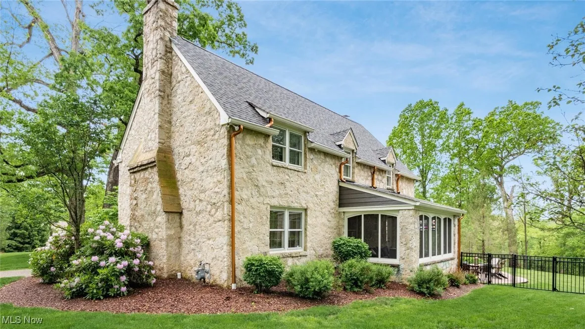 Back of house featuring a sunroom, stone siding, a chimney, and roof with shingles