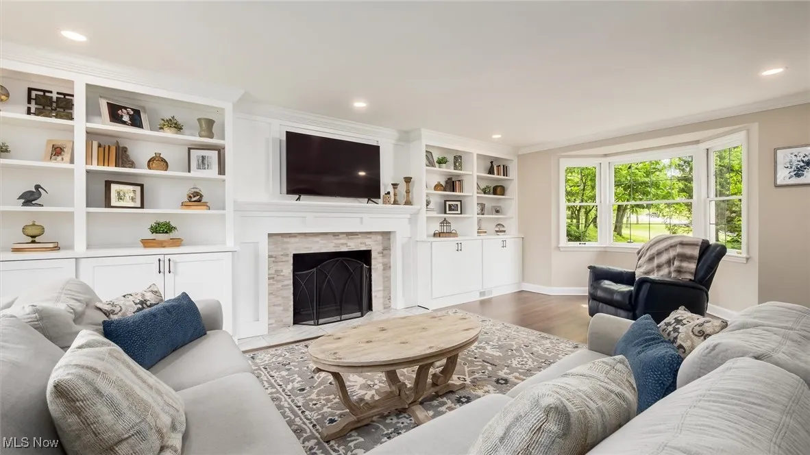 Living area with baseboards, wood finished floors, recessed lighting, a stone fireplace, and crown molding