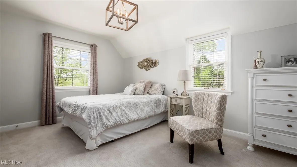 Bedroom featuring vaulted ceiling, light carpet, baseboards, and a chandelier