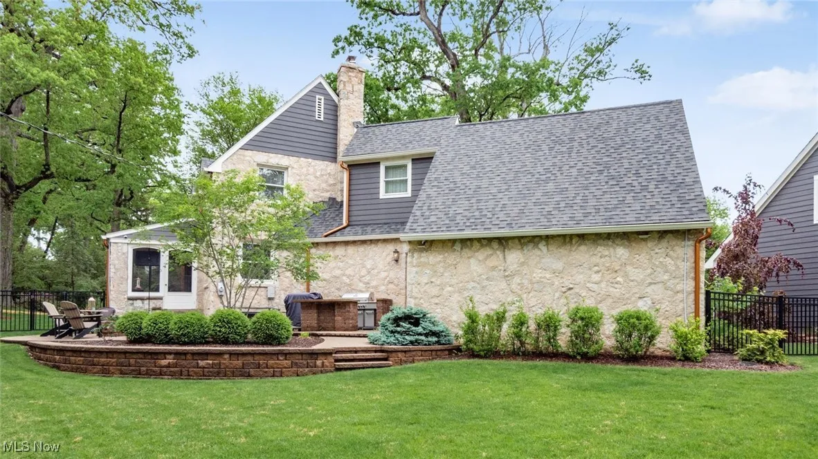 Rear view of house with stone siding, a chimney, roof with shingles, and a patio