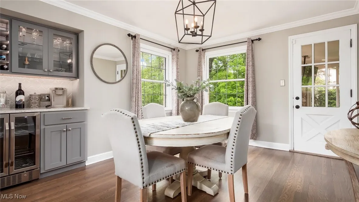Dining space featuring wine cooler, baseboards, a chandelier, a dry bar, and dark wood finished floors
