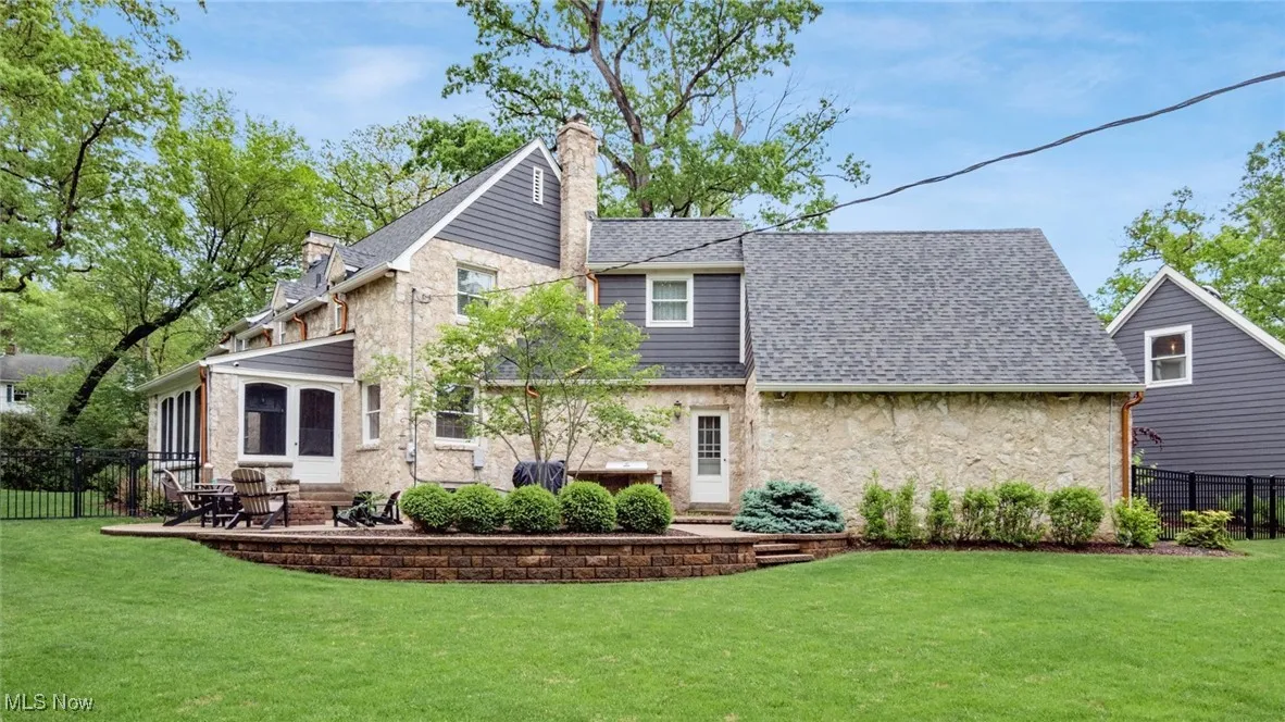 Rear view of property featuring stone siding, a chimney, a patio area, and a shingled roof