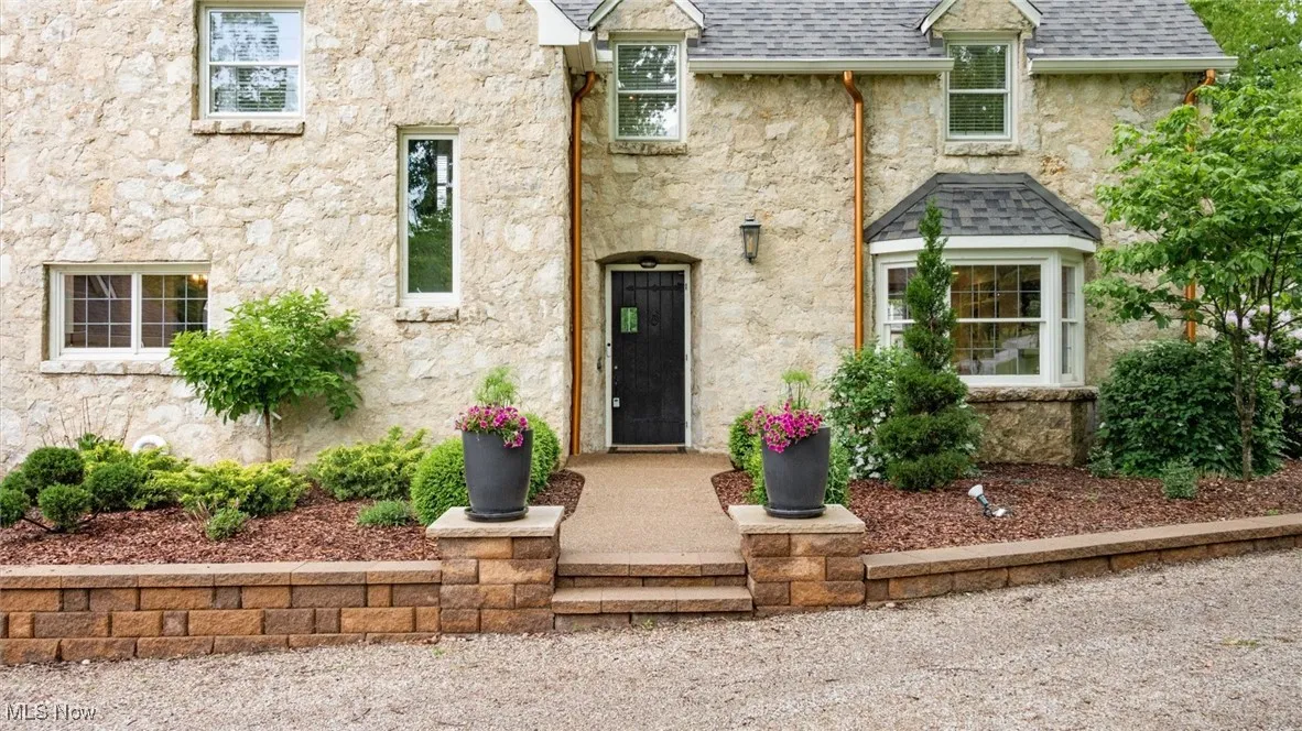 View of front facade with stone siding, roof with shingles, and stucco siding