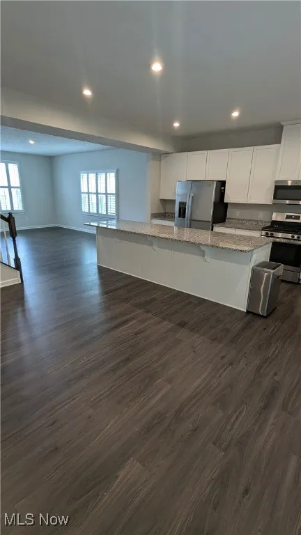 Kitchen featuring stainless steel appliances, dark wood-style flooring, recessed lighting, a kitchen breakfast bar, and white cabinets