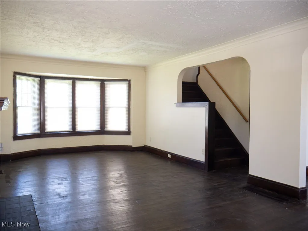 Unfurnished living room featuring a textured ceiling, dark wood-type flooring, healthy amount of natural light, baseboards, and ornamental molding