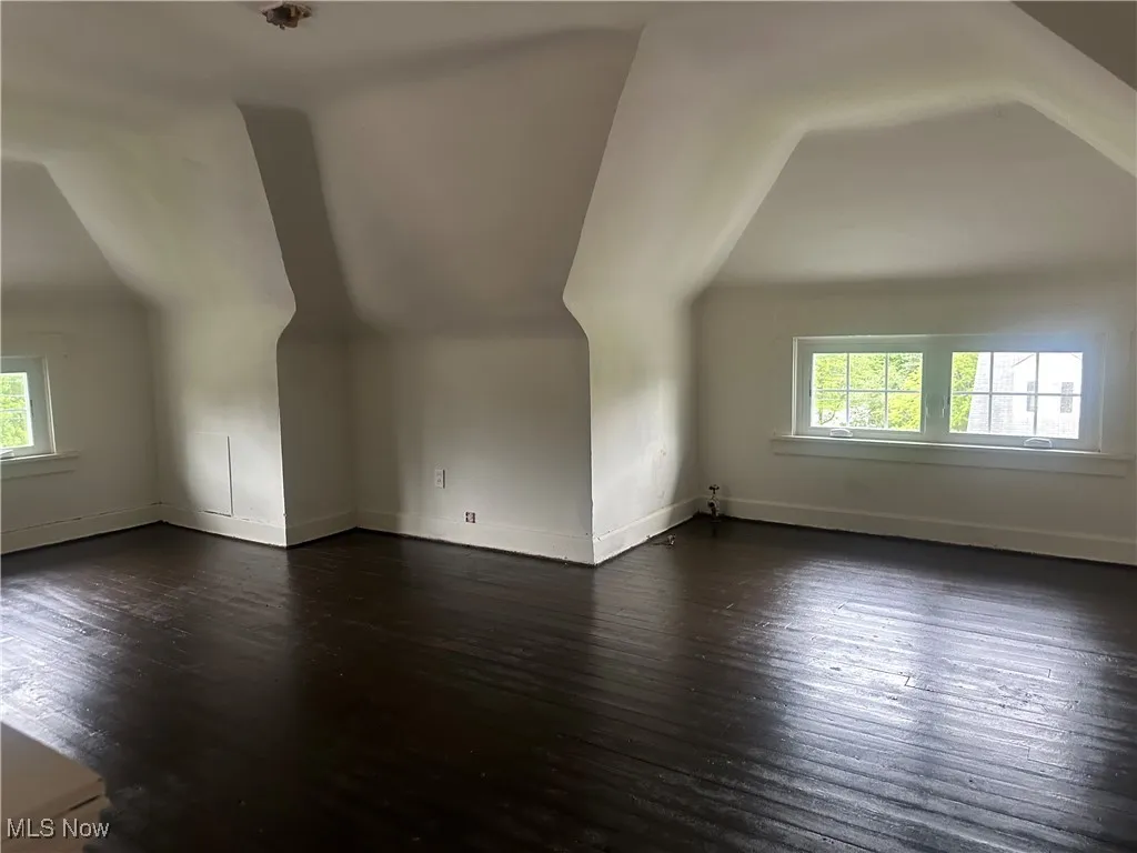 Additional living space featuring vaulted ceiling, healthy amount of natural light, dark wood-style floors, and baseboards