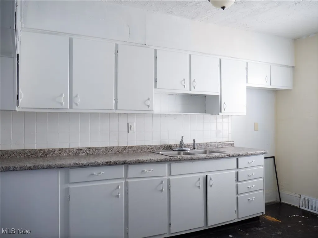 Kitchen featuring a sink, tasteful backsplash, white cabinets, and a textured ceiling