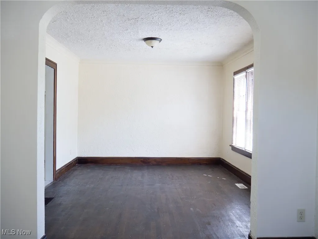 Empty room featuring arched walkways, wood finished floors, a textured ceiling, baseboards, and crown molding