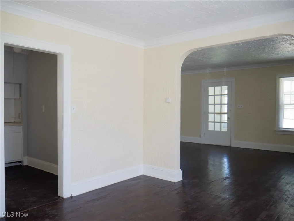 Spare room featuring arched walkways, wood finished floors, ornamental molding, and baseboards