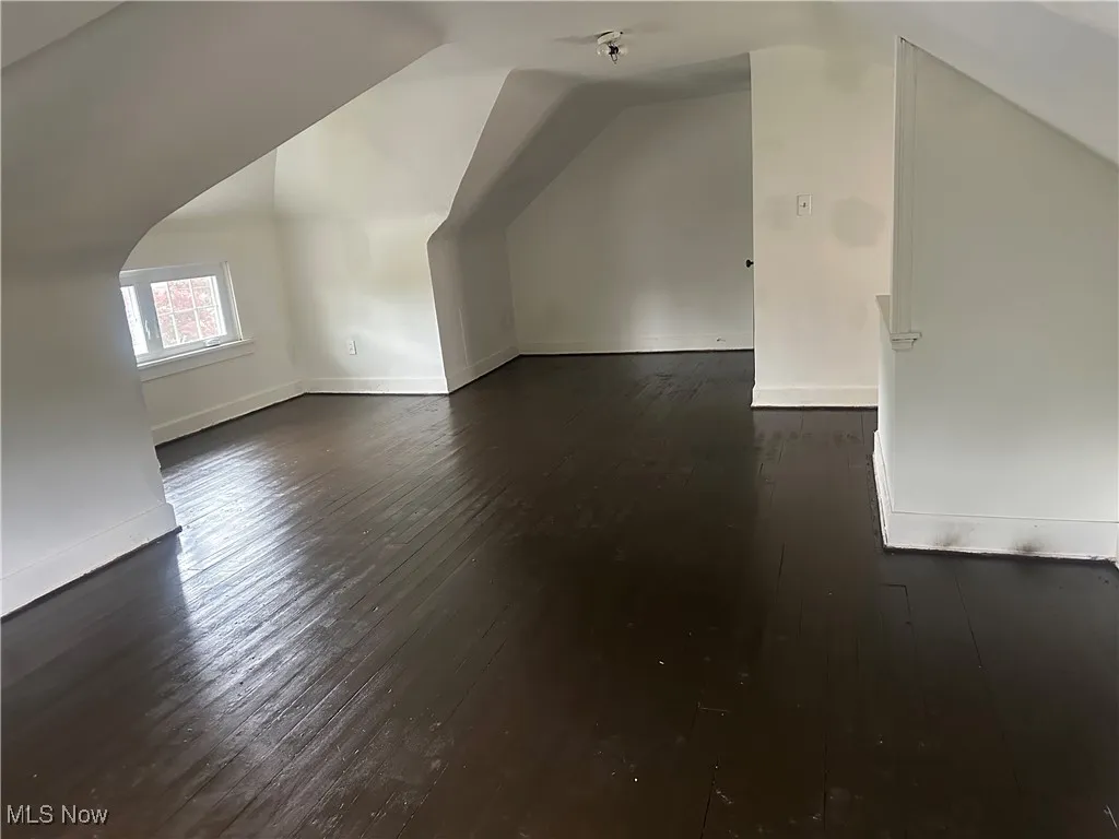 Bonus room with dark wood-style flooring, vaulted ceiling, and baseboards