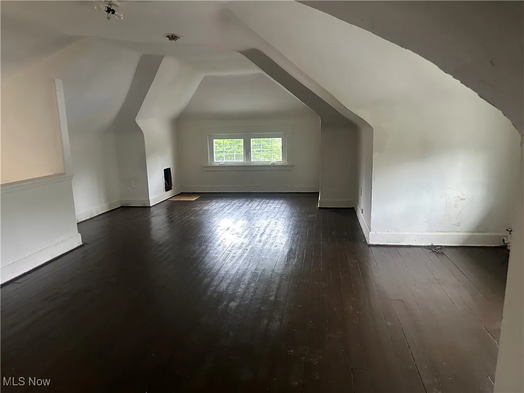 Bonus room with dark wood-type flooring, lofted ceiling, and baseboards