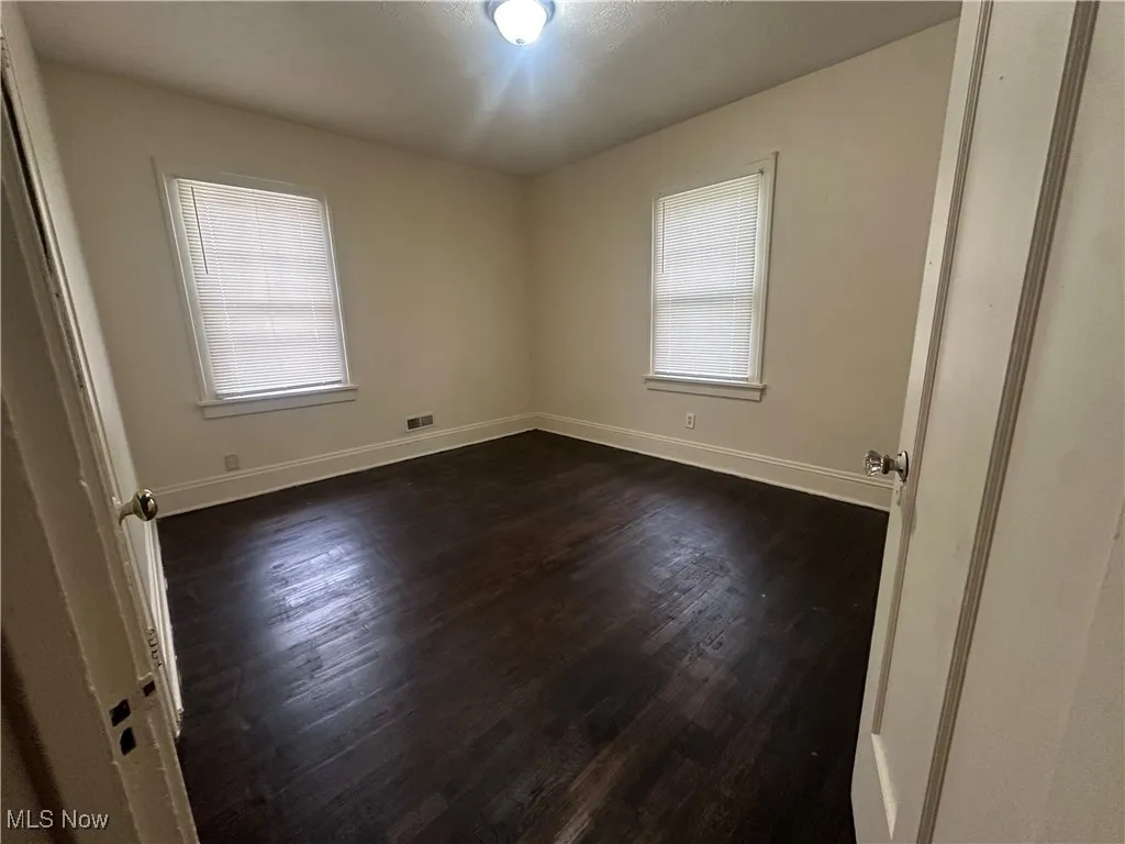 Spare room featuring plenty of natural light, dark wood-style floors, and baseboards