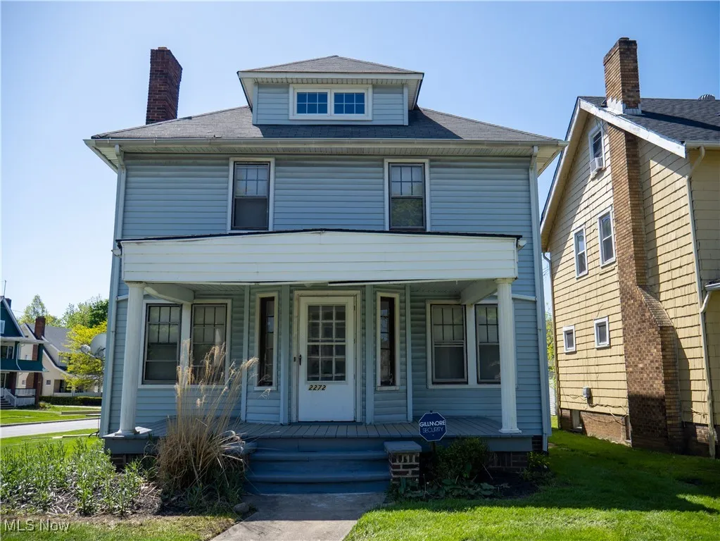 American foursquare style home with covered porch, a front lawn, and a chimney