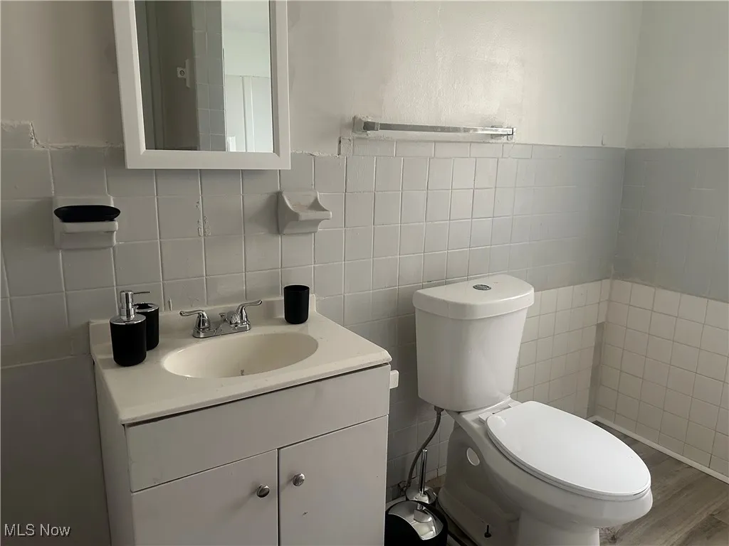 Bathroom with tile walls, toilet, vanity, and wood finished floors