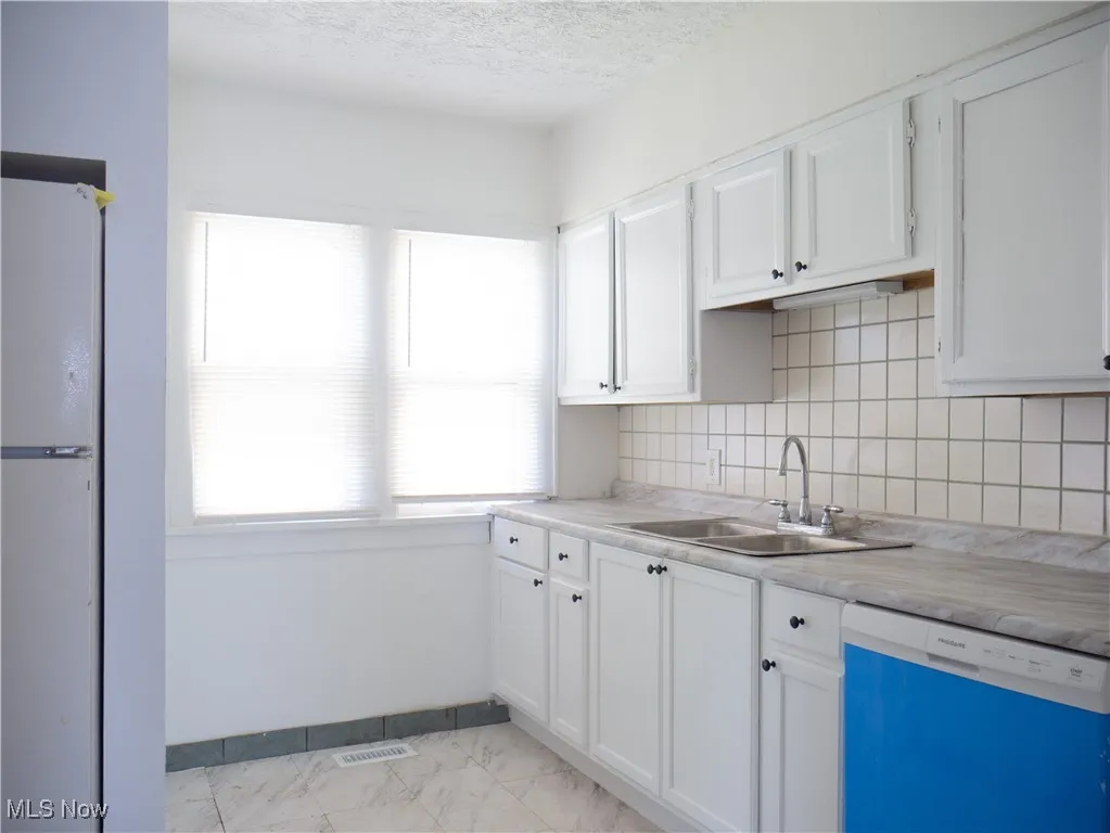 Kitchen with dishwashing machine, a sink, white cabinets, light countertops, and a textured ceiling