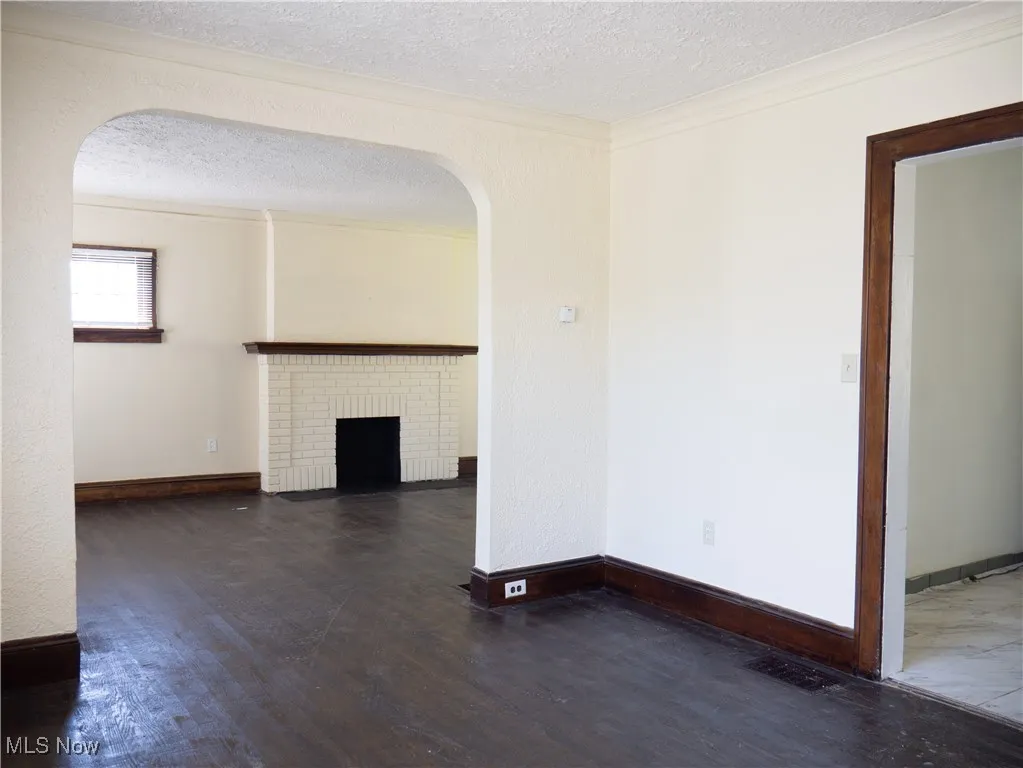 Unfurnished living room with arched walkways, a textured ceiling, wood finished floors, a fireplace, and baseboards