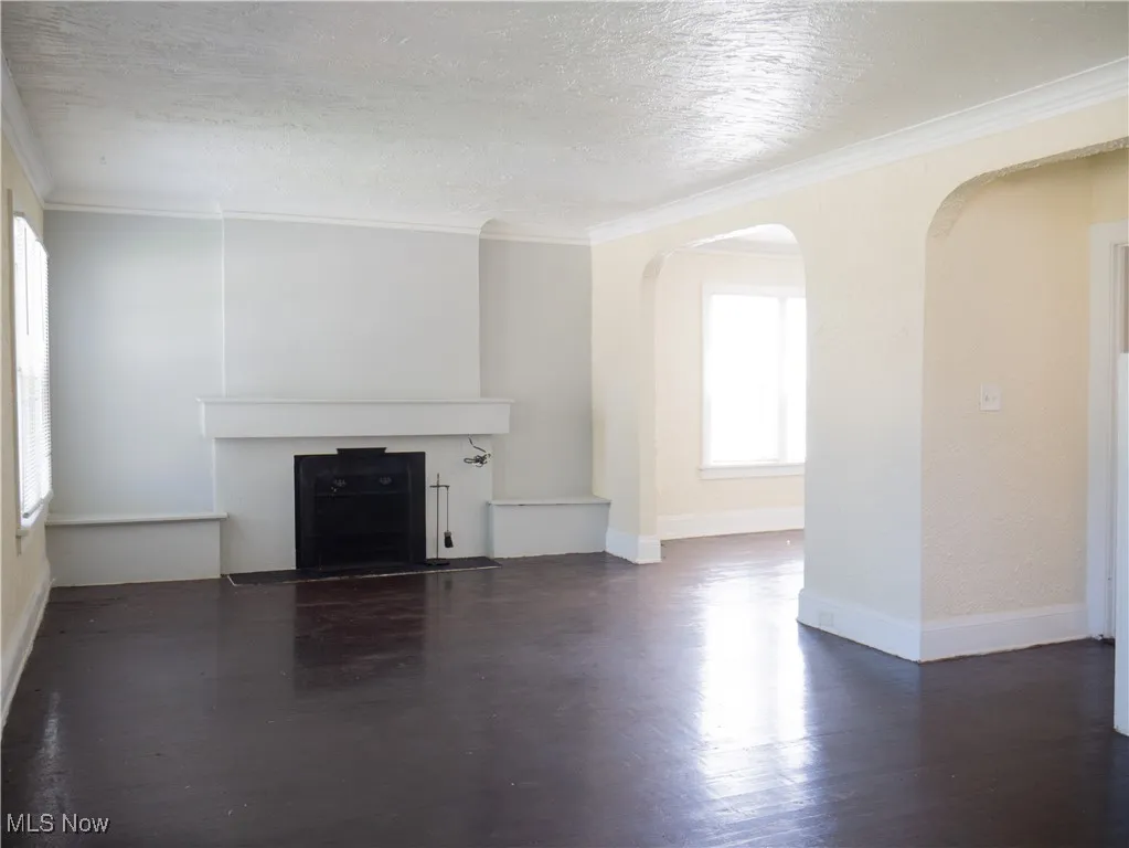 Unfurnished living room with healthy amount of natural light, arched walkways, a textured ceiling, a fireplace with flush hearth, and wood finished floors