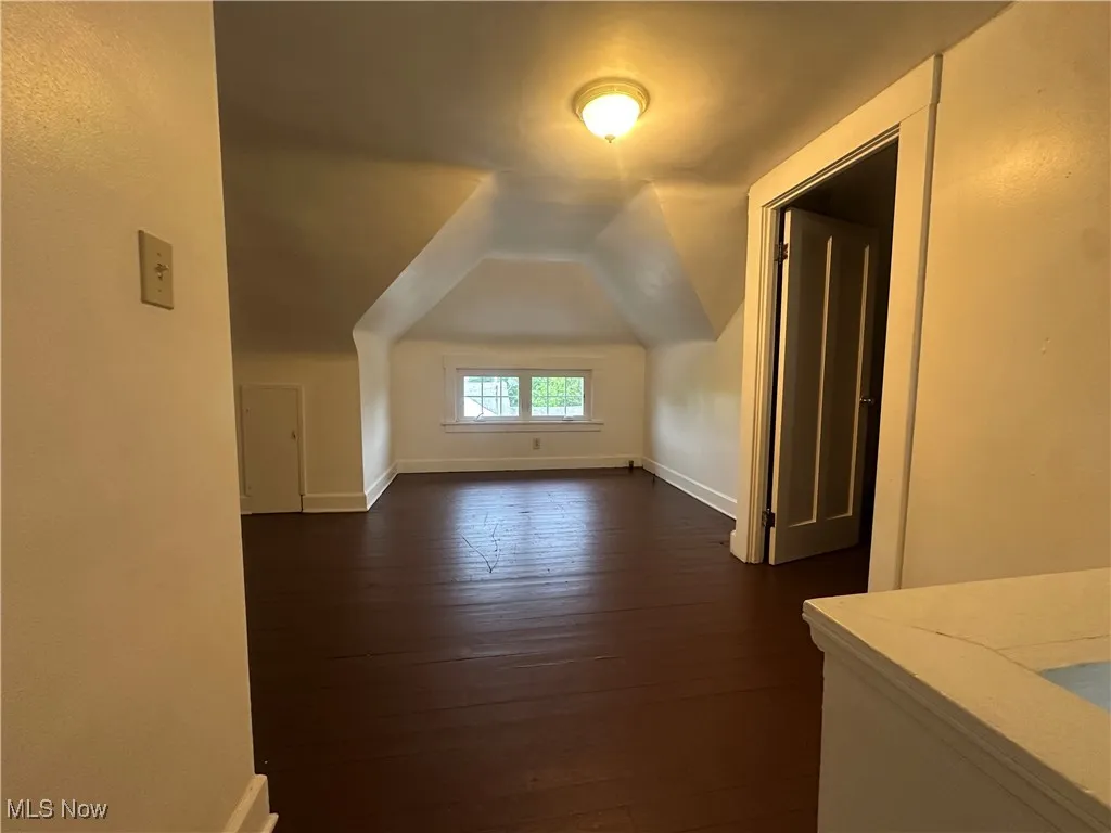 Additional living space with dark wood finished floors, baseboards, and vaulted ceiling