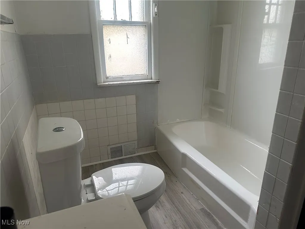 Bathroom with tile walls, toilet, and wood finished floors