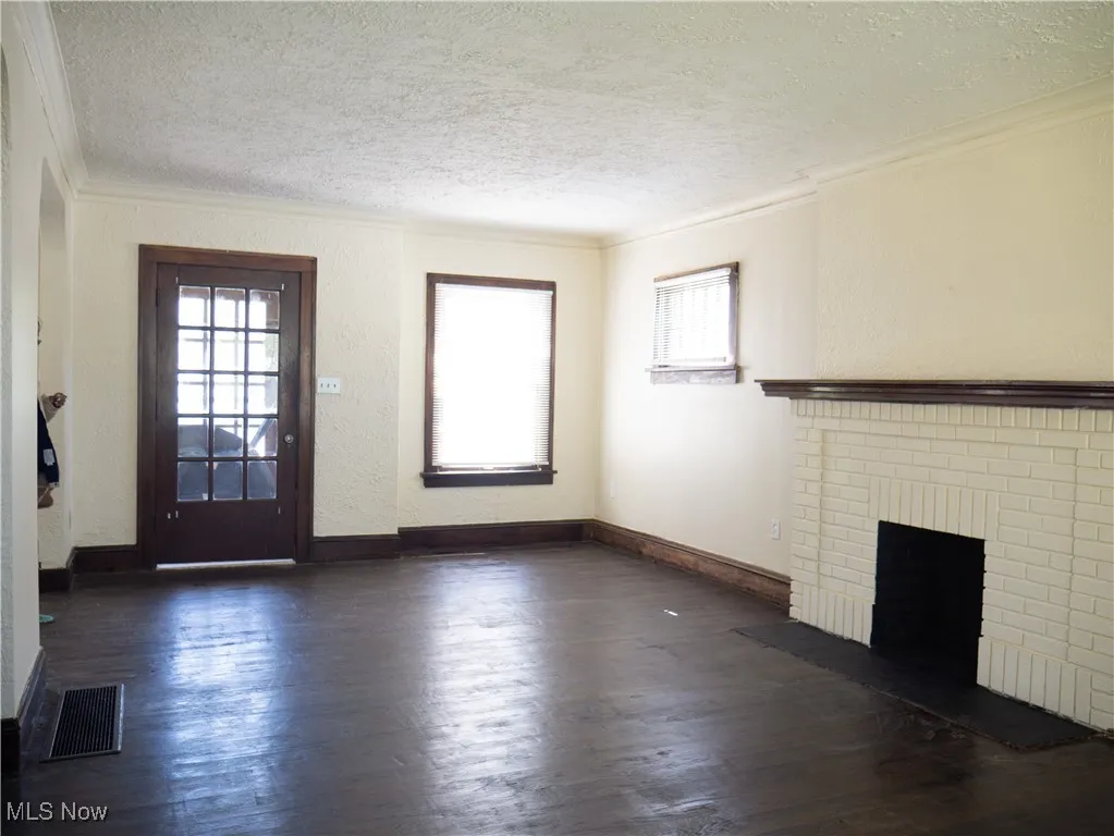 Unfurnished living room featuring ornamental molding, a textured ceiling, healthy amount of natural light, dark wood finished floors, and a fireplace