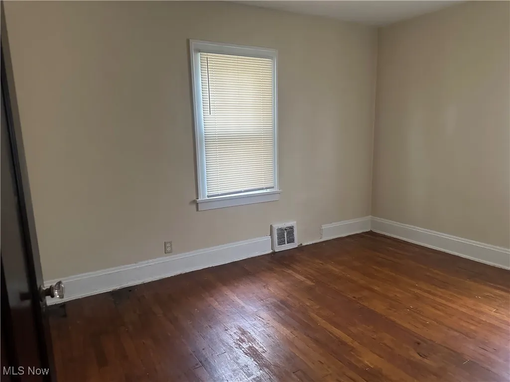 Spare room featuring dark wood-style flooring and baseboards