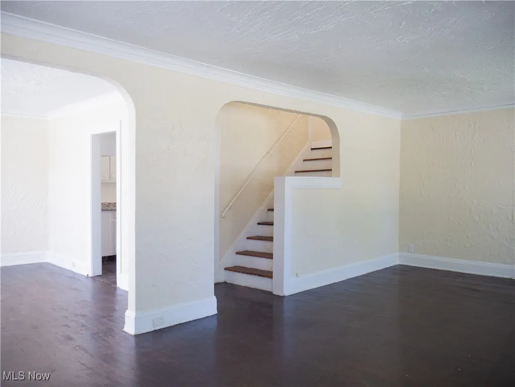 Empty room with wood finished floors, arched walkways, a textured ceiling, stairs, and baseboards