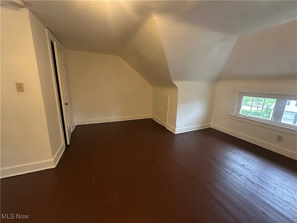 Bonus room featuring dark wood finished floors, lofted ceiling, and baseboards