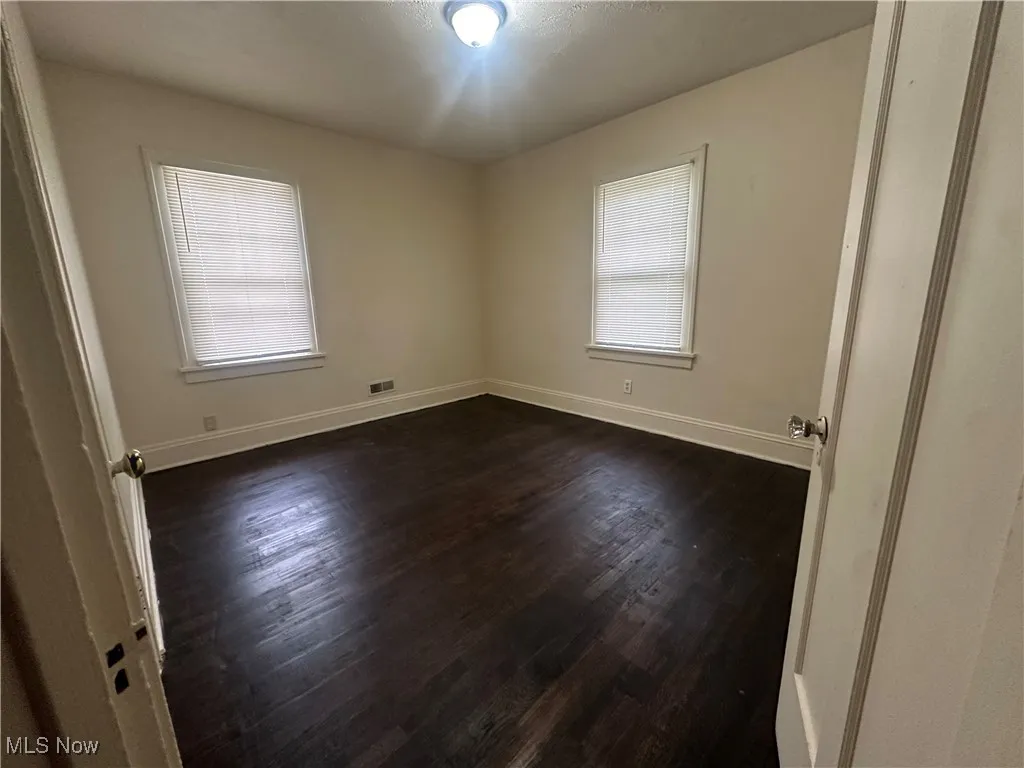 Unfurnished room featuring plenty of natural light, dark wood-type flooring, and baseboards