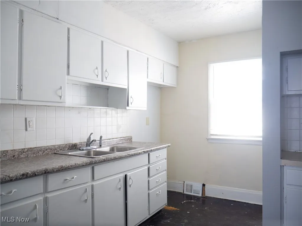 Kitchen with a sink, decorative backsplash, white cabinets, baseboards, and a textured ceiling