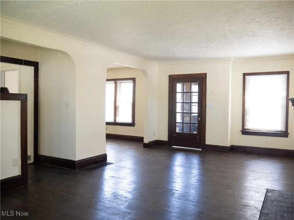 Entryway featuring a textured ceiling, ornamental molding, arched walkways, dark wood finished floors, and baseboards