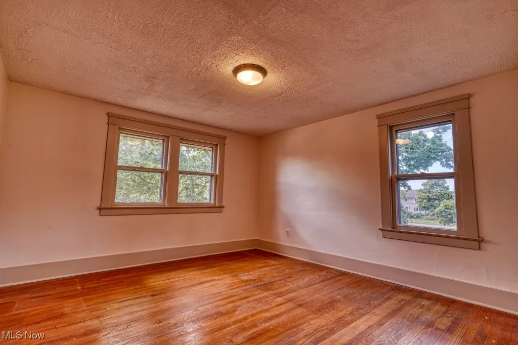 Spare room featuring a textured ceiling, light wood finished floors, healthy amount of natural light, and baseboards