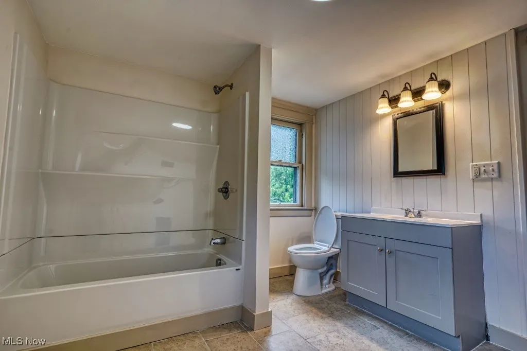 Bathroom with toilet, washtub / shower combination, vanity, and baseboards