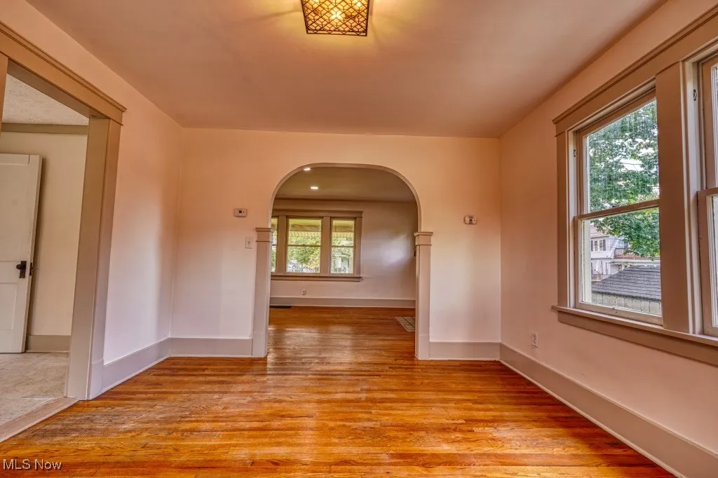 Empty room featuring arched walkways, light wood finished floors, and baseboards