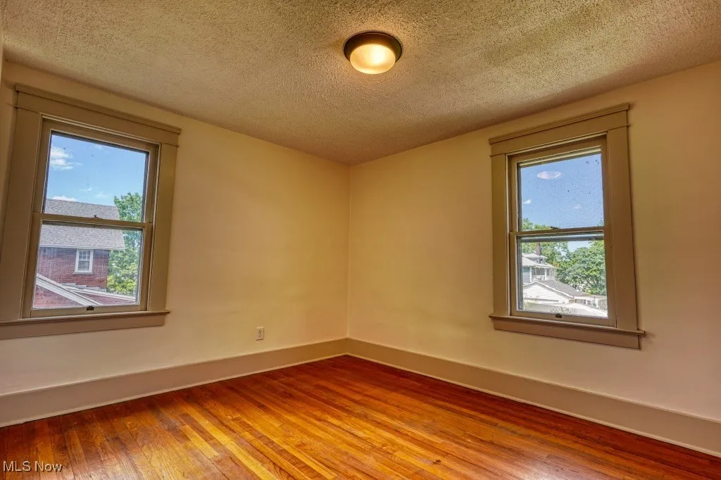 Empty room featuring plenty of natural light, hardwood / wood-style flooring, a textured ceiling, and baseboards