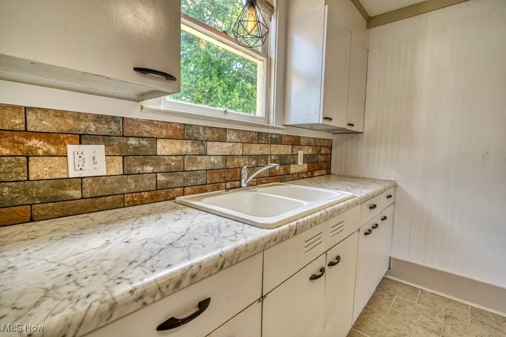 Kitchen featuring a sink, light countertops, backsplash, and white cabinetry