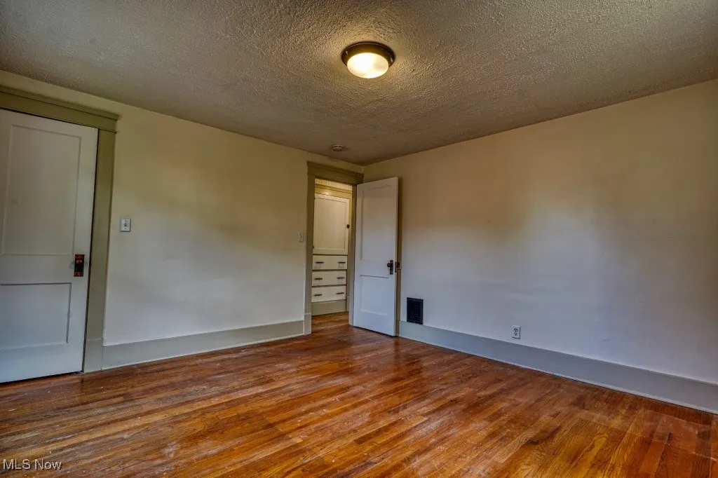 Empty room with wood finished floors, a textured ceiling, and baseboards