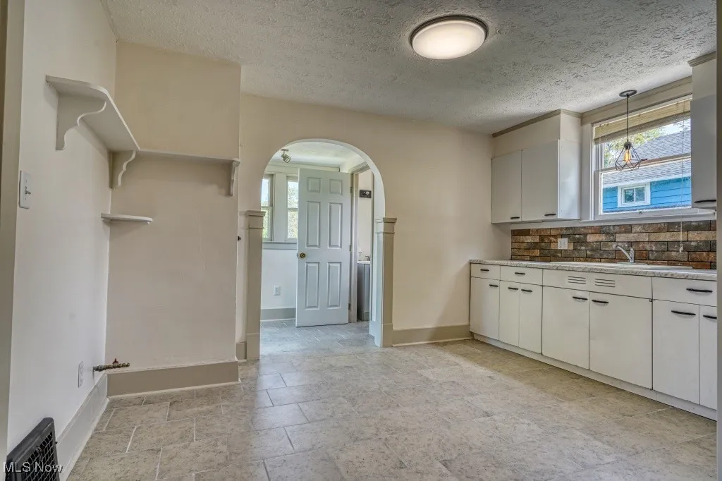 Kitchen featuring arched walkways, healthy amount of natural light, tasteful backsplash, baseboards, and a textured ceiling