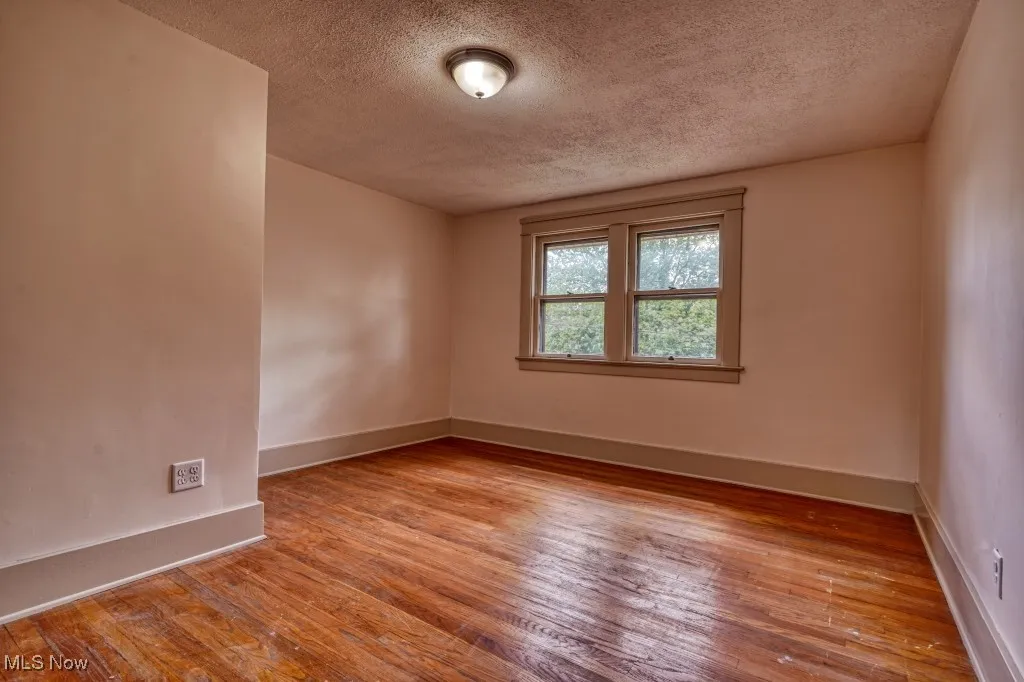 Empty room featuring a textured ceiling, hardwood / wood-style floors, and baseboards