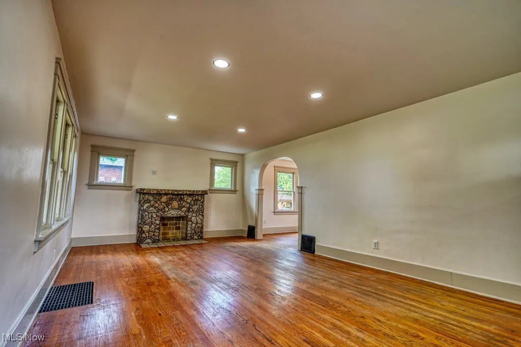 Unfurnished living room with arched walkways, wood finished floors, baseboards, a stone fireplace, and recessed lighting