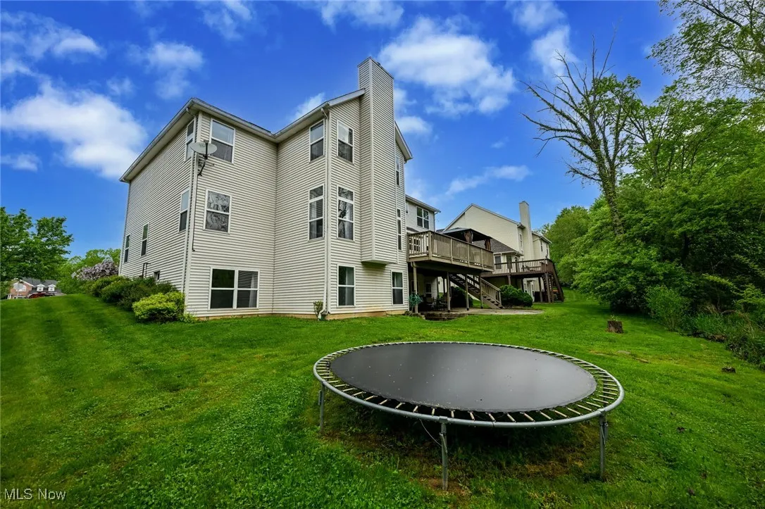 Rear view of house with a trampoline, a wooden deck, stairs, a chimney, and a lawn
