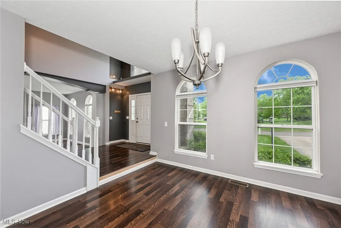 Unfurnished dining area featuring a chandelier, wood finished floors, plenty of natural light, baseboards, and a textured ceiling