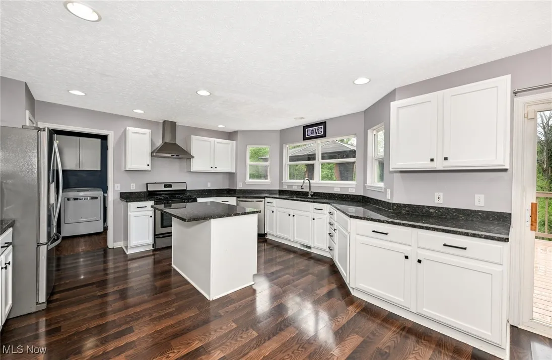 Kitchen with stainless steel appliances, wall chimney exhaust hood, washer / clothes dryer, healthy amount of natural light, and recessed lighting