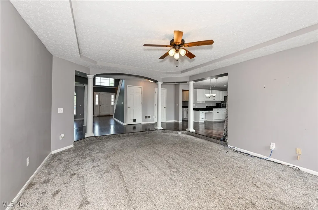 Unfurnished living room featuringdecorative columns, a textured ceiling, baseboards, a ceiling fan, and arched walkways