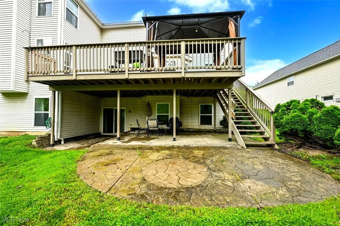 Back of house featuring a wooden deck, a patio area, stairway, and an a lawn