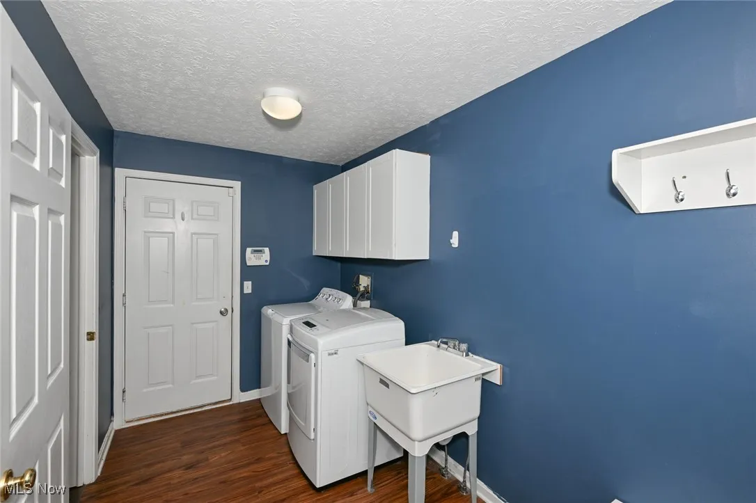 Washroom featuring separate washer and dryer, cabinet space, dark wood finished floors, leads to garage